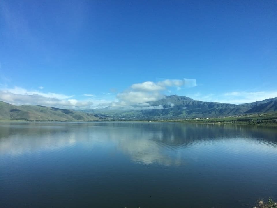 El dique La Angostura espejado, con los cerros del valle y nubes bajas al fondo