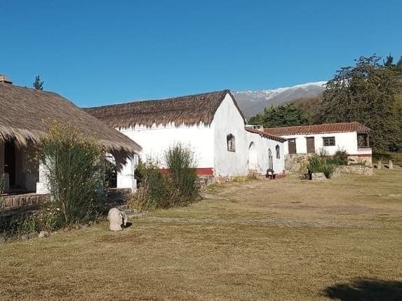 El casco de estancia del museo, con su techo de paja y la capilla, frente a los cerros nevados